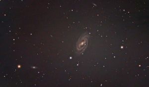 Messier 109 occupies an area of 7.6 by 4.7 arc minutes of apparent sky, corresponding to a linear diameter of 180,000 light years. The galaxy can be seen in large binoculars in exceptionally good conditions. 4-inch telescopes show a hazy streak of light, while 6-inch instruments reveal the galaxy’s nucleus surrounded by nebulosity. Only the galaxy’s bright central region with the bar can be seen visually. Messier 109 is located only 40 arc minutes southeast of the magnitude 2.44 star Phecda, Gamma Ursae Majoris, the star marking the bowl of the Big Dipper toward the handle. The best time of year to observe M109 is during the spring.